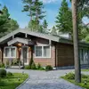 A charming wooden cabin with a gray roof surrounded by lush green trees and a paved pathway.